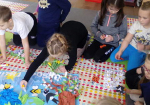 Dzieci zgromadzone wokół pracy plastycznej na piankowym dywanie.